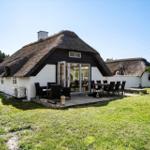 Haus mit Strohdach, Terrasse und Garten. Ein Hund liegt auf der Terrasse.