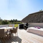 Terrasse mit Tisch, Stühlen, Grill und Liege unter strohgedecktem Dach.