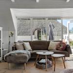Ein Wohnzimmer mit braunem Sofa, Glaswand und Blick auf einen Garten.