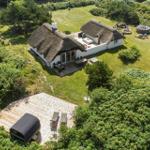 Dänische Ferienhaus mit Strohdach, Terrasse und Garten. Daneben steht eine moderne Sauna auf Holzterrasse.