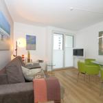 Wohn- und Essbereich mit Sofa, grünen Stühlen und Glas-tisch.