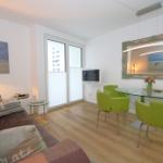 Wohn- und Essbereich mit grünen Stühlen, Glas-Tisch und Fernseher.