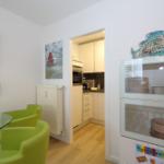 Essbereich mit grünen Stühlen und Glasplatte. Küche im Hintergrund. Glasvitrine mit Geschirr.