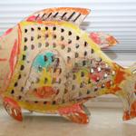 Farbenfroher Fisch aus Metall mit Lochmuster steht auf einer Fensterbank.