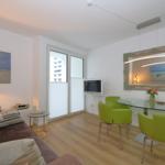 Wohnzimmer mit Esstisch, grünen Stühlen und Fernseher an der Wand.