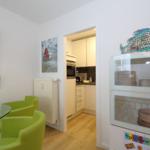 Essbereich mit grünen Stühlen und Glasplatte. Küche im Hintergrund. Glasvitrine mit Geschirr und Fischdekoration.