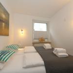 Schlafzimmer mit Bett, Wandbild und Fenster mit Jalousie.