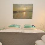 Schlafzimmer mit Bett, Kissen und Wandbild. Beleuchtung und Schrank sind sichtbar.