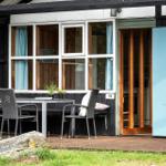 House with terrace, table, chairs, and blue door. Windows with light blue curtains.