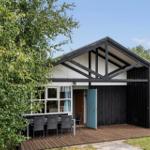 House with terrace, table and chairs, surrounded by trees and grass.