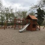 Wooden playground with slide, climbing frame, and swing on gravel surface