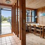 Dining area with wooden table, chairs, and windows. Passage to terrace with wooden planks.