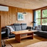 Living room with wooden wall, two gray sofas, and wooden table. Large windows with view of forest.