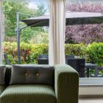 Green sofa with cushions overlooks terrace with umbrella and garden.