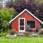 Red wooden house with terrace and chairs in the garden