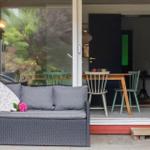 Patio with gray sofa, table and chairs. Red wooden frame and outdoor lighting.