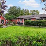 Red house with garden and terrace. Surrounded by trees and shrubs.