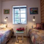 Zwei Betten mit Quiltdecken stehen im Raum. Fenster, Wandlampen und Holzwand sind sichtbar.