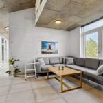 Wohnzimmer mit grauem Sofa, Holztisch und großen Fenstern.