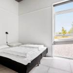 Schlafzimmer mit weißem Bett und großem Fenster zur Außensicht.