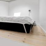 Schlafzimmer mit Bett, Holzboden und Wandbeleuchtung.