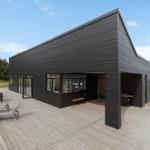 Moderne schwarze Villa mit großem Holzterrasse, Grillbereich und Außensitzgelegenheiten.