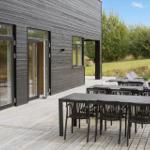 Terrasse mit Tischen und Stühlen vor modernem Haus mit Holzfassade.