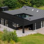 Moderne schwarze Villa mit großem Holzdeck und Garten.
