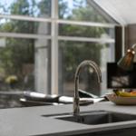 Kitchen faucet over stainless steel sink with fruit bowl on countertop.