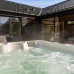 A steaming hot tub in front of a house with dark wood and large windows.