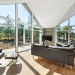 Living room with large windows, sofa and chair. Wooden floor and stone roof.