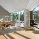 Dining area with wooden table and chairs. Large windows with forest view. Leather armchair and ottoman.