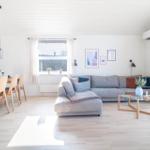 Wohn- und Essbereich mit Sofa, Tisch und Stühlen. Weiße Wände und Holzboden.