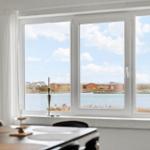 Großes Fenster mit Blick auf Wasser und Häuser. Tisch und Stühle im Vordergrund.