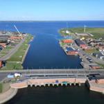 Aerial view of a coastal village with harbor, bridge, and wind turbines.