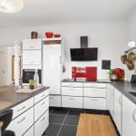 Moderne Küche mit weißen Schränken, schwarzen Arbeitsflächen und rotem Backsplash.