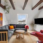 Wohnzimmer mit grauem Sofa, rotem Sessel und Holzbalken an der Decke.
