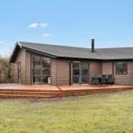 Modern wooden cabin with terrace, grill, and large windows.
