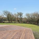 Wooden terrace with view of green lawn and trees in the background.