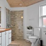 Bathroom with shower, toilet, and sink. Wooden ceiling and window with daylight.