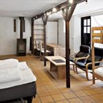 Room with multiple sleeping areas, wooden beds, seating, and wood stove.