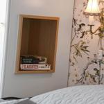 Bettkante mit Holzregal, Blumenwand und Wandlampe.