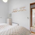 Schlafzimmer mit Bett, Kleiderständer und Fenster. Durchgang zur Badewanne.