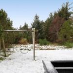 Schneebedeckter Spielplatz mit Schaukel im Wald.