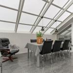 Dining area with table, chairs, and recliner under glass roof.