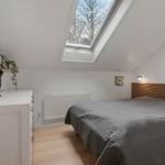 Schlafzimmer mit Dachschrägen, Dachfenster und Holzboden. Bett mit grauer Bettwäsche und weißer Kommode.