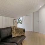 Schwarzes Sofa mit Felldecke, weiße Holzwände und Holzboden im Wohnbereich.