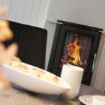 Ein Kamin mit brennendem Feuer und eine Tischplatte mit Tassen und Schale.