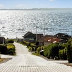 Path leads to houses by water with view of a harbor.