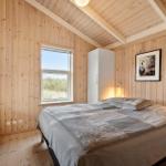 Schlafzimmer mit Holzwänden, Bett und Fenster zum Blick auf Grasland.